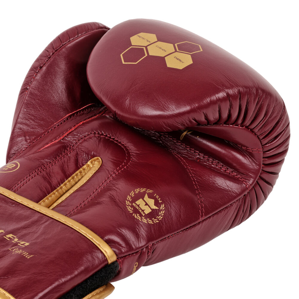Détail macro du gant de boxe Montana X-FIGHT Evo Legend : grain du cuir bordeaux, hexagones dorés et surpiqûres or de la manchette.