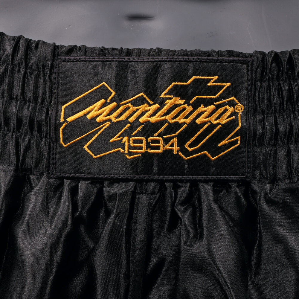 Détail de la ceinture du short de boxe Montana MULTIBOX NewCode : logo Montana 1934 brodé en doré sur la large bande élastique noire.