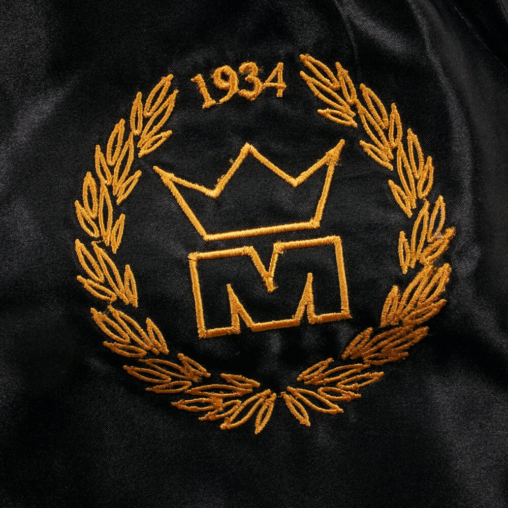 Détail macro du blason doré à la couronne daté 1934, brodé sur la jambe du short de boxe Montana MULTIBOX NewCode en satin noir.