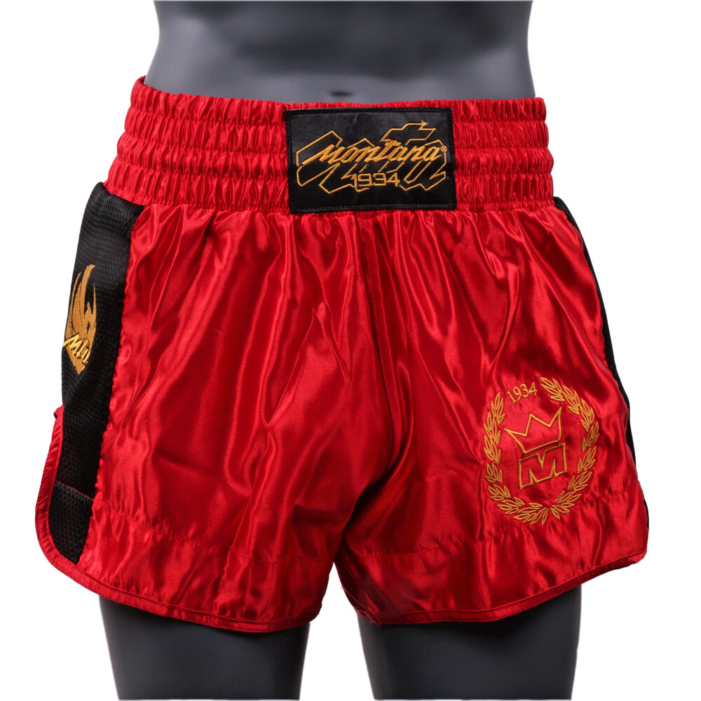 Short de boxe rouge Montana MUAY THAI NewCode en satin polyester, porté et vu de face, avec la large bande élastique de ceinture et le blason doré à la couronne.