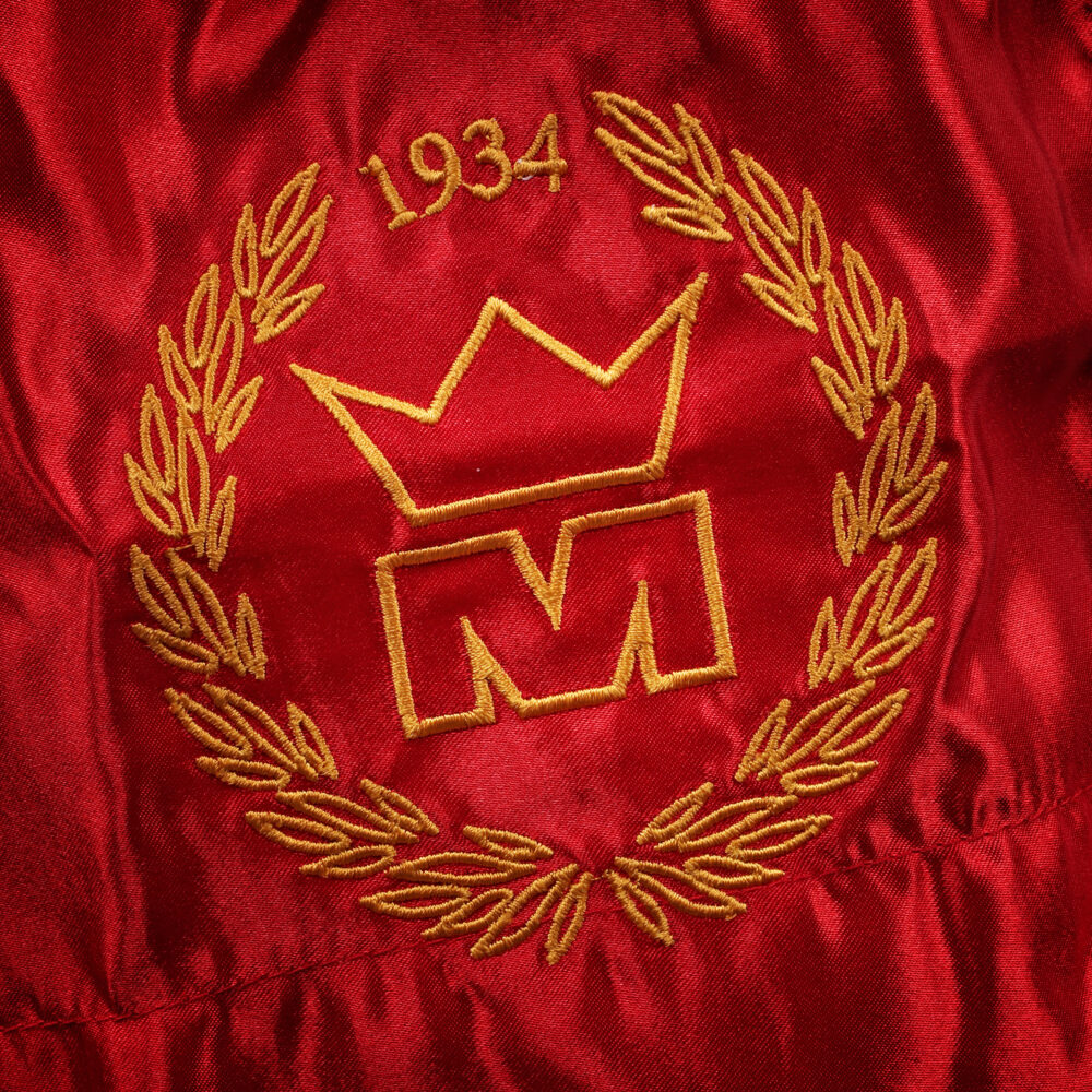 Détail macro du blason doré à la couronne daté 1934, brodé sur la jambe du short de boxe Montana MUAY THAI NewCode en satin rouge.