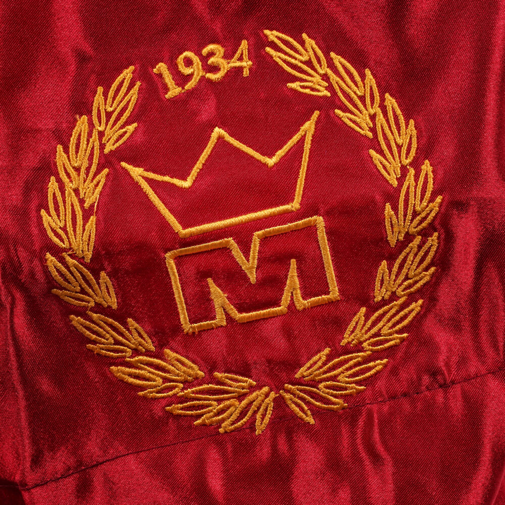 Détail macro du blason doré à la couronne daté 1934, brodé sur la jambe du short de boxe Montana MUAY THAI NewCode Legend en satin bordeaux.