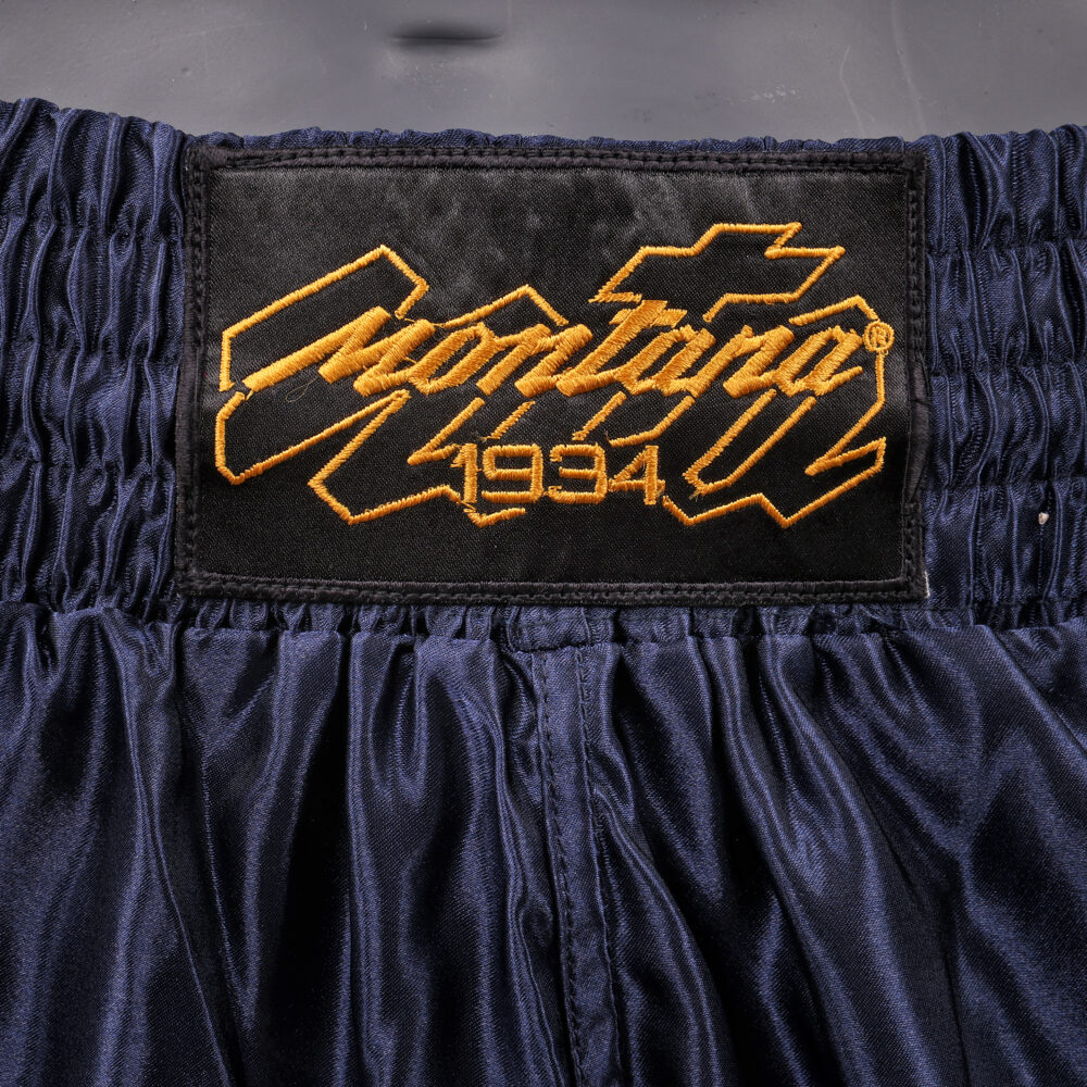 Détail de la ceinture du short de boxe Montana MUAY THAI NewCode Poseidon : logo Montana 1934 brodé en doré sur la bande élastique navy.