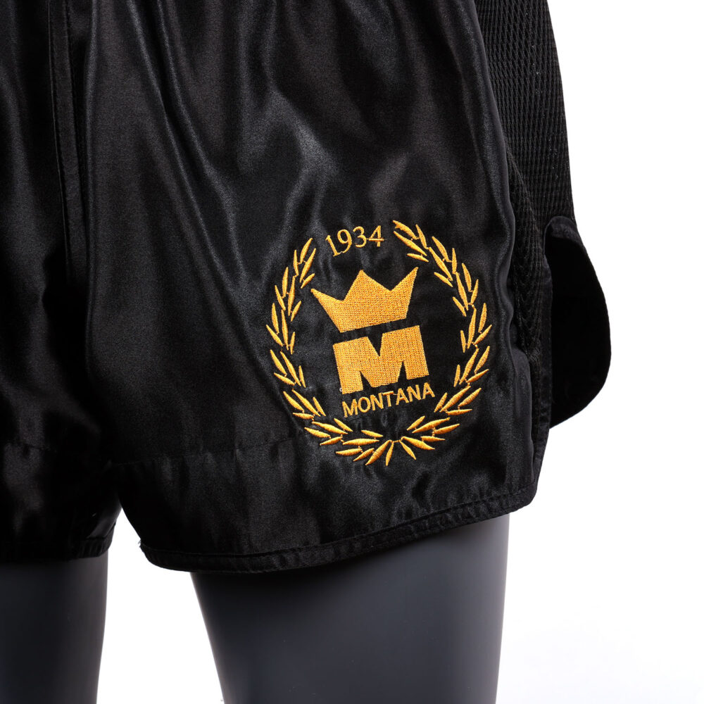 Short Muay Thai noir NewCode en satin polyester, avec bande latérale mesh VENTIL’AIR pour une meilleure ventilation, large ouverture et ceinture élastique.