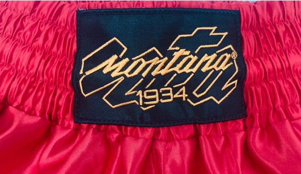 Short Muay Thai rouge NewCode en satin polyester, avec bande latérale mesh VENTIL’AIR pour une meilleure ventilation, large ouverture et ceinture élastique.