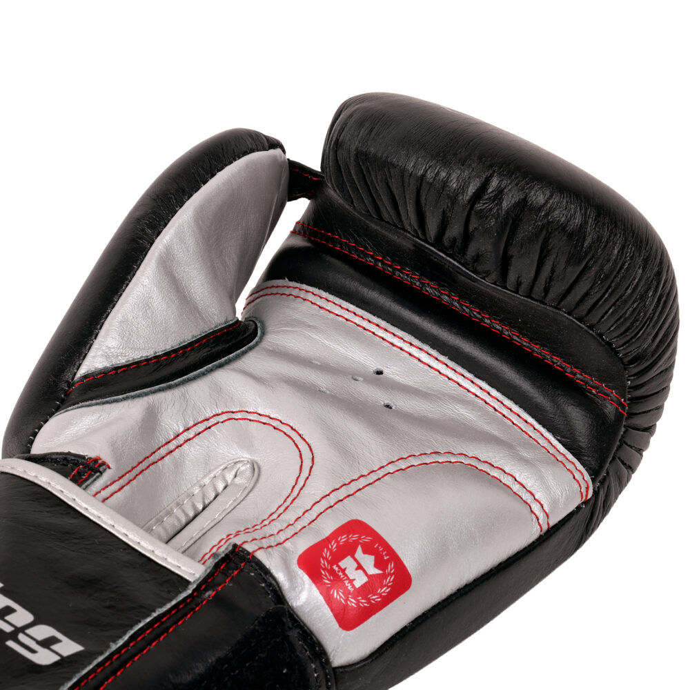 Détail macro du gant de boxe Montana SPARRING Identity : contraste du cuir noir et de la paume gris argent, surpiqûres rouges et étiquette de la marque.