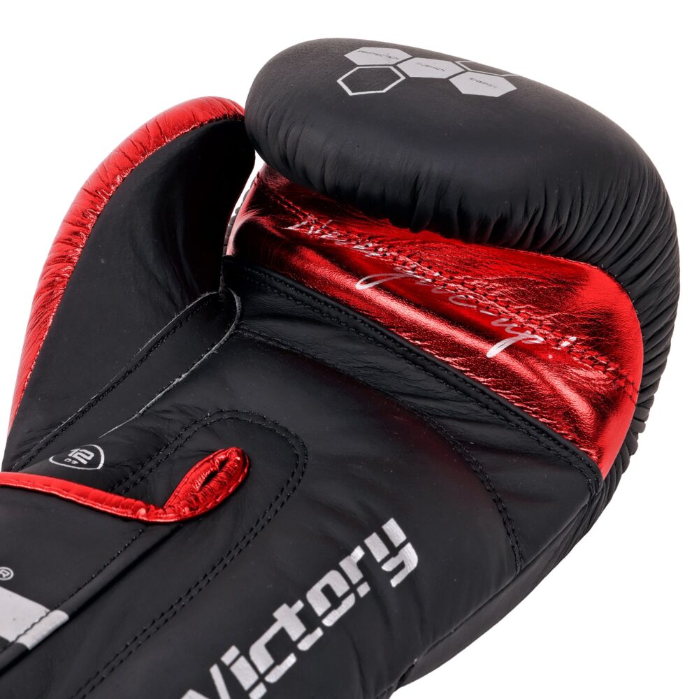 Détail macro du gant de boxe Montana VICTORY Identity : contraste entre le cuir de vachette noir mat et l'empiècement rouge métallisé, lettrage Victory et surpiqûres.